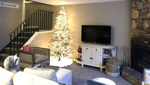Ein Wohnzimmer mit Weihnachtsbaum, Kamin, Treppe und Fernseher.