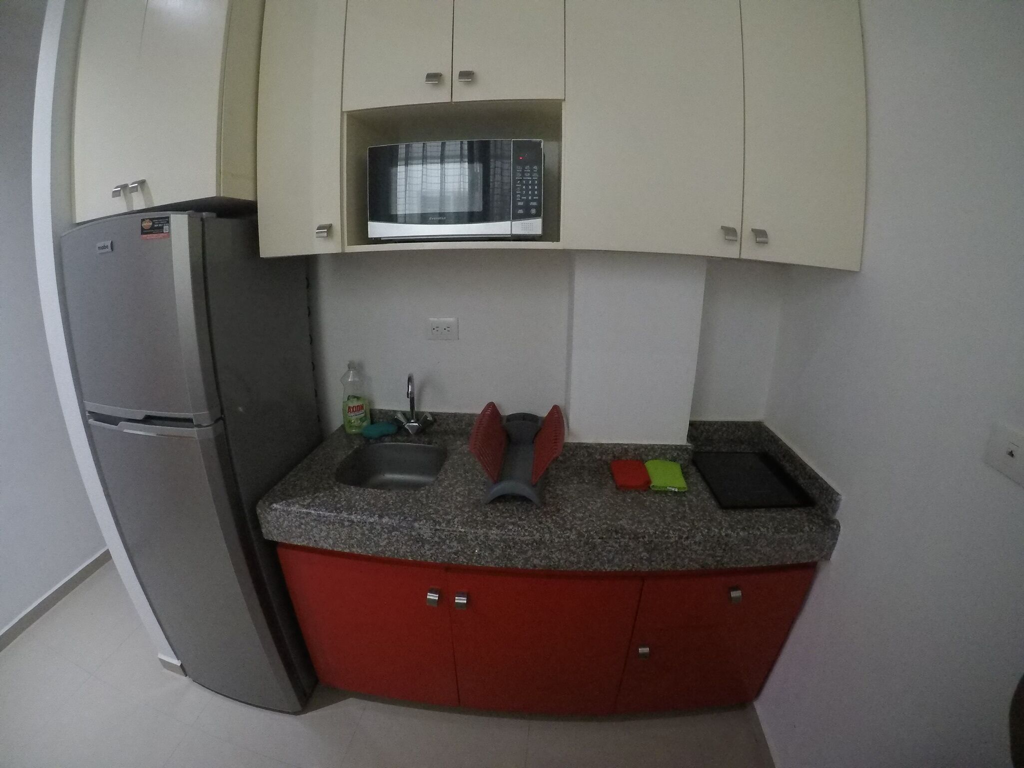 A compact kitchen with a refrigerator, microwave, sink, and red cabinets.