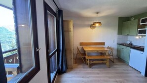 A compact kitchen with a wooden table and bench, a window with curtains, and a view of greenery outside.