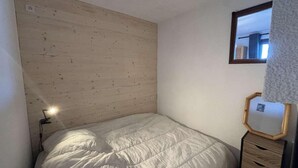 A bedroom with a wooden headboard, a bed with white bedding, a bedside lamp, a wooden nightstand with drawers, and a mirror on the wall.