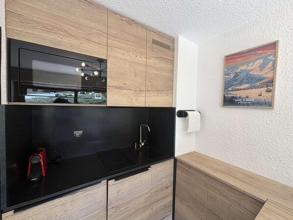 A compact kitchen with a black countertop, wooden cabinets, a built-in oven, and a sink.