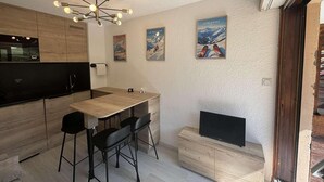 Moderni keittiö, jossa on puinen pöytä, mustat tuolit ja musta televisio puisen kaapin päällä.