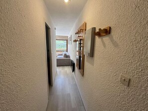 Un couloir étroit avec un plancher en bois, une porte sur la gauche et une fenêtre au fond.