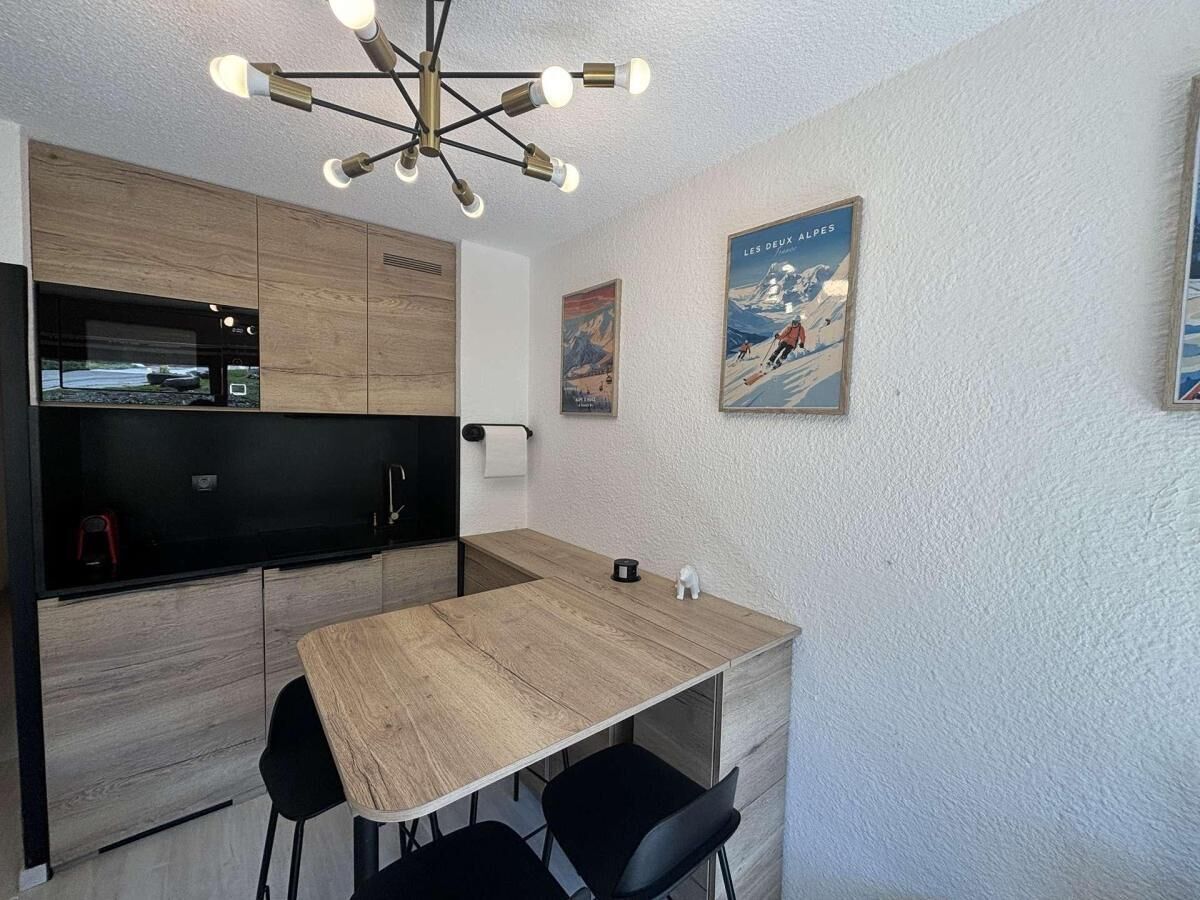 Una cucina compatta con un tavolo in legno, sedie nere e un lampadario moderno.