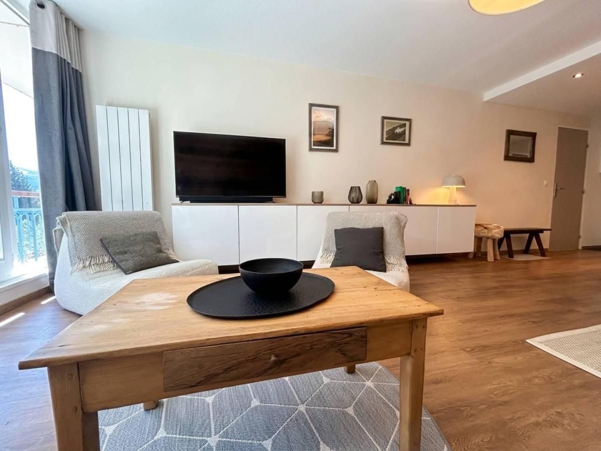 Un salon moderne avec une table à manger en bois, un téléviseur à écran plat fixé au mur et un canapé agrémenté de coussins.