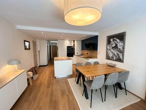 A modern kitchen with white cabinets, a wooden dining table, and grey chairs.