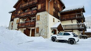 Un immeuble en bois à plusieurs étages, doté de balcons, d’une base en pierre et d’un toit recouvert de neige.