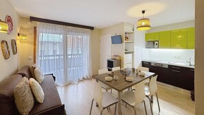 Un appartement moderne comprenant un coin repas, un canapé, une cuisine avec des meubles verts et un téléviseur fixé au mur.