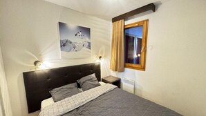 Un lit bien fait, recouvert d’une couvre-lit à motifs géométriques, avec une tête de lit, des lampes de chevet, une table de chevet et un tableau représentant un cheval en montagne, accroché au mur.