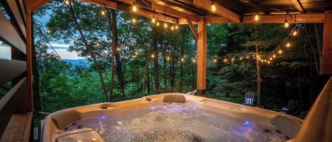 Un jacuzzi con vistas a un bosque y montañas, rodeado de vigas de madera y luces colgantes.