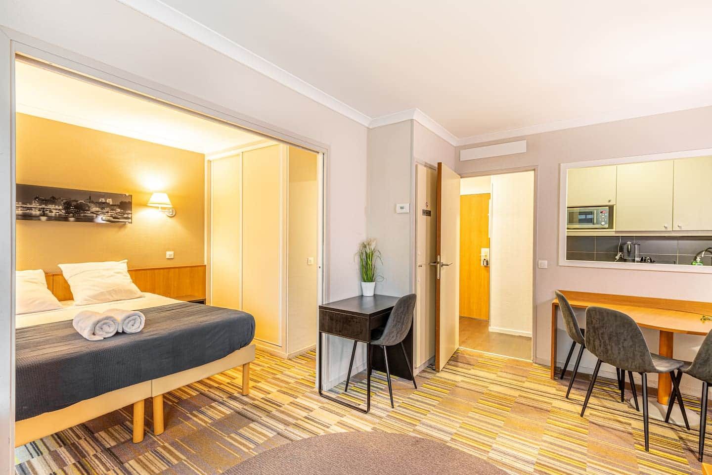 Una habitación de hotel con cama, escritorio, silla y una pequeña cocina.
