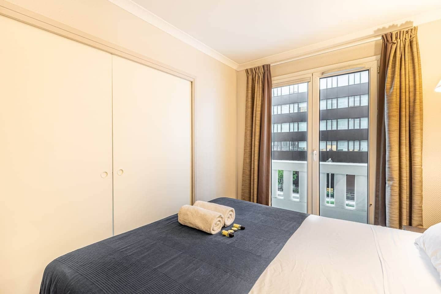 Een hotelkamer met een bed, een kledingkast, een raam met gordijnen en uitzicht op gebouwen.