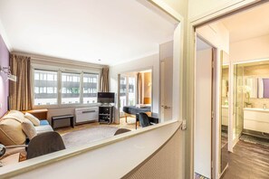 Habitación de hotel con sofá, televisión, escritorio y vistas a la ciudad a través de amplias ventanas.