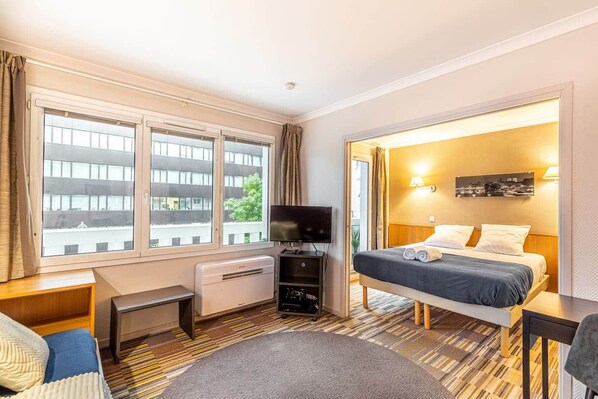 Habitación de hotel con cama, televisor, escritorio y ventana con vistas a edificios.