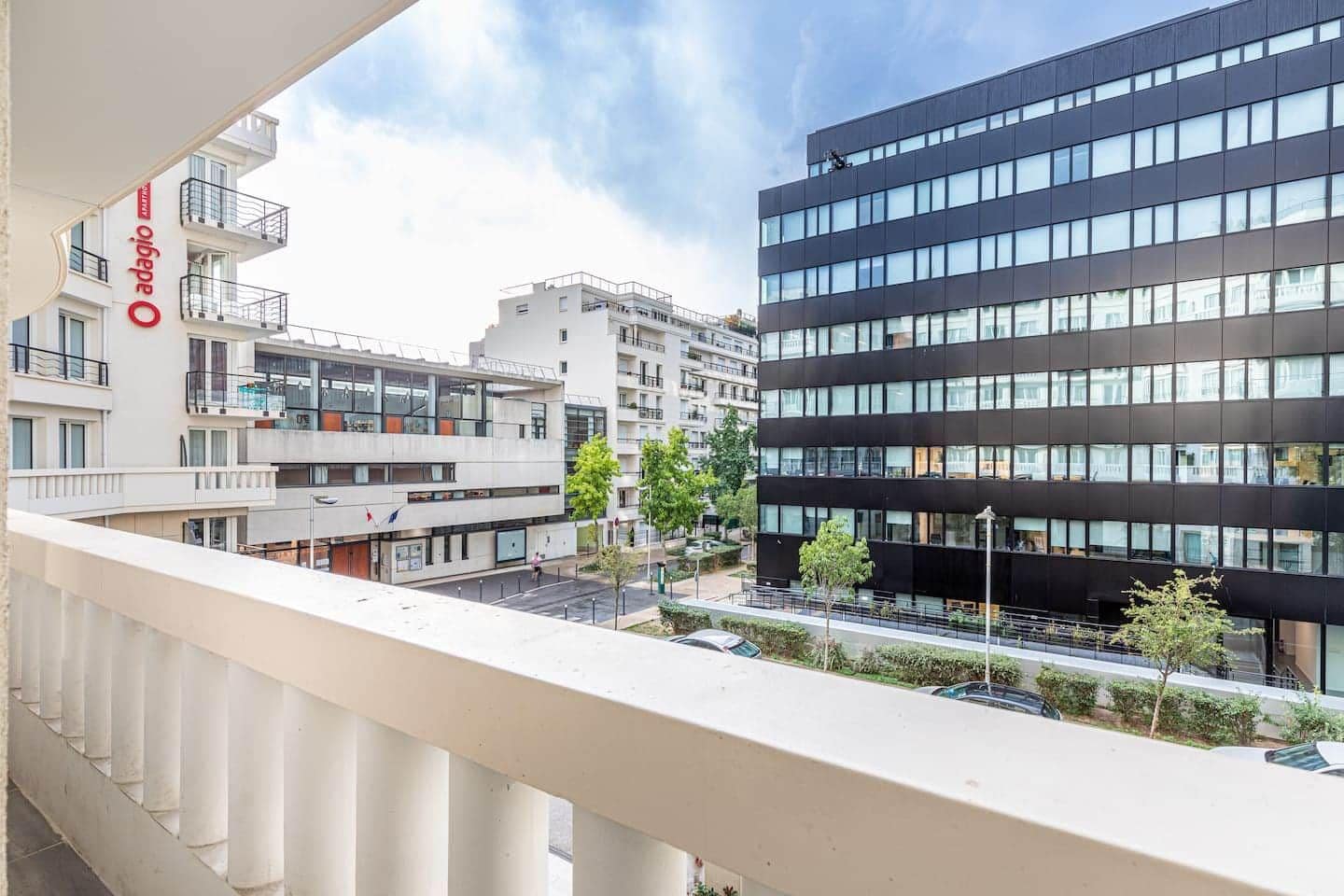 Un edificio moderno con balcones, cielo despejado y zona de estacionamiento.