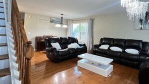 Ein großzügiges Wohnzimmer mit einer Holztreppe, zwei schwarzen Ledersofas, einem weißen Couchtisch und einer Kristallleuchter.