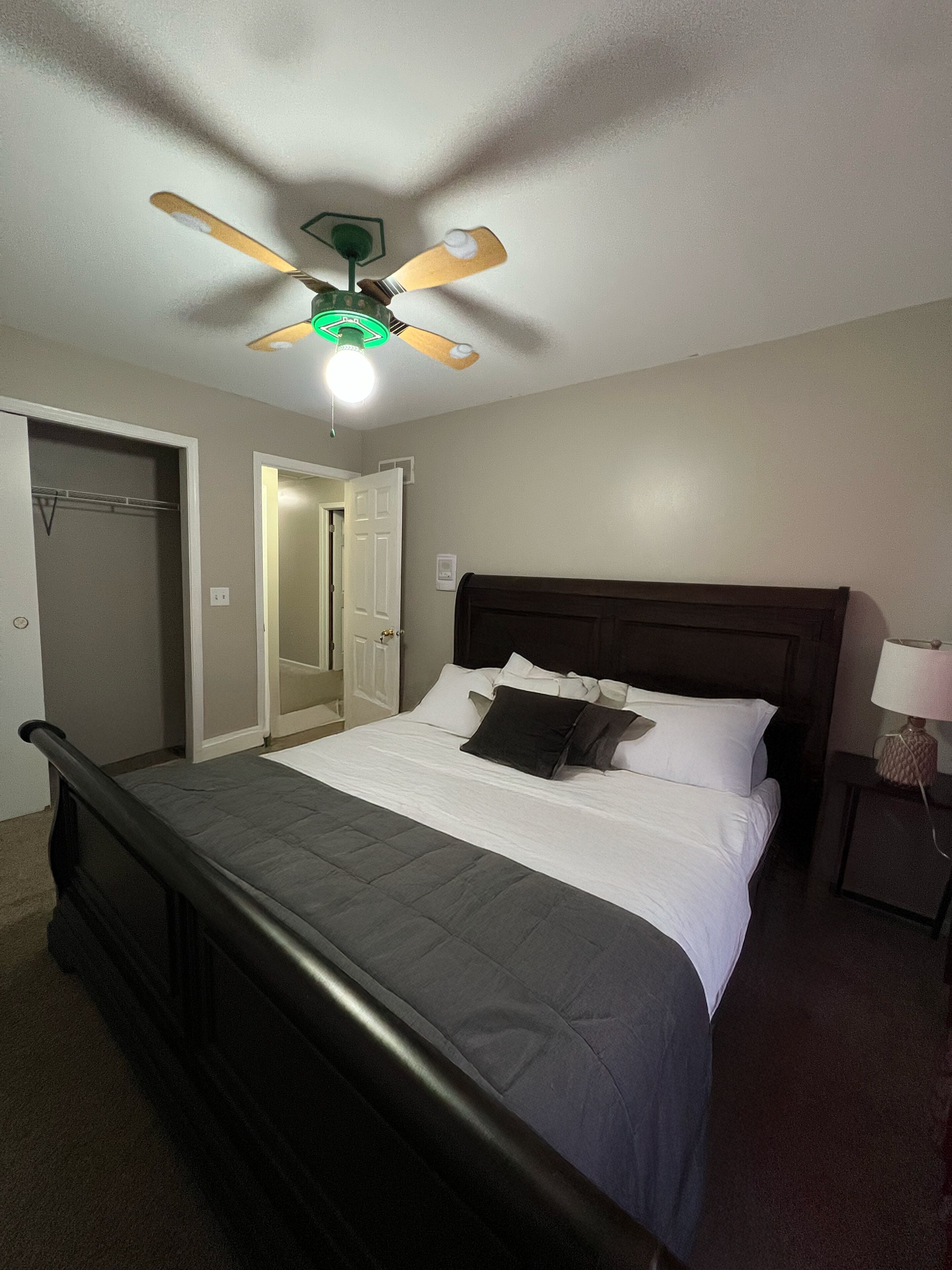 A bedroom with a bed, a ceiling fan, a nightstand, and a lamp.