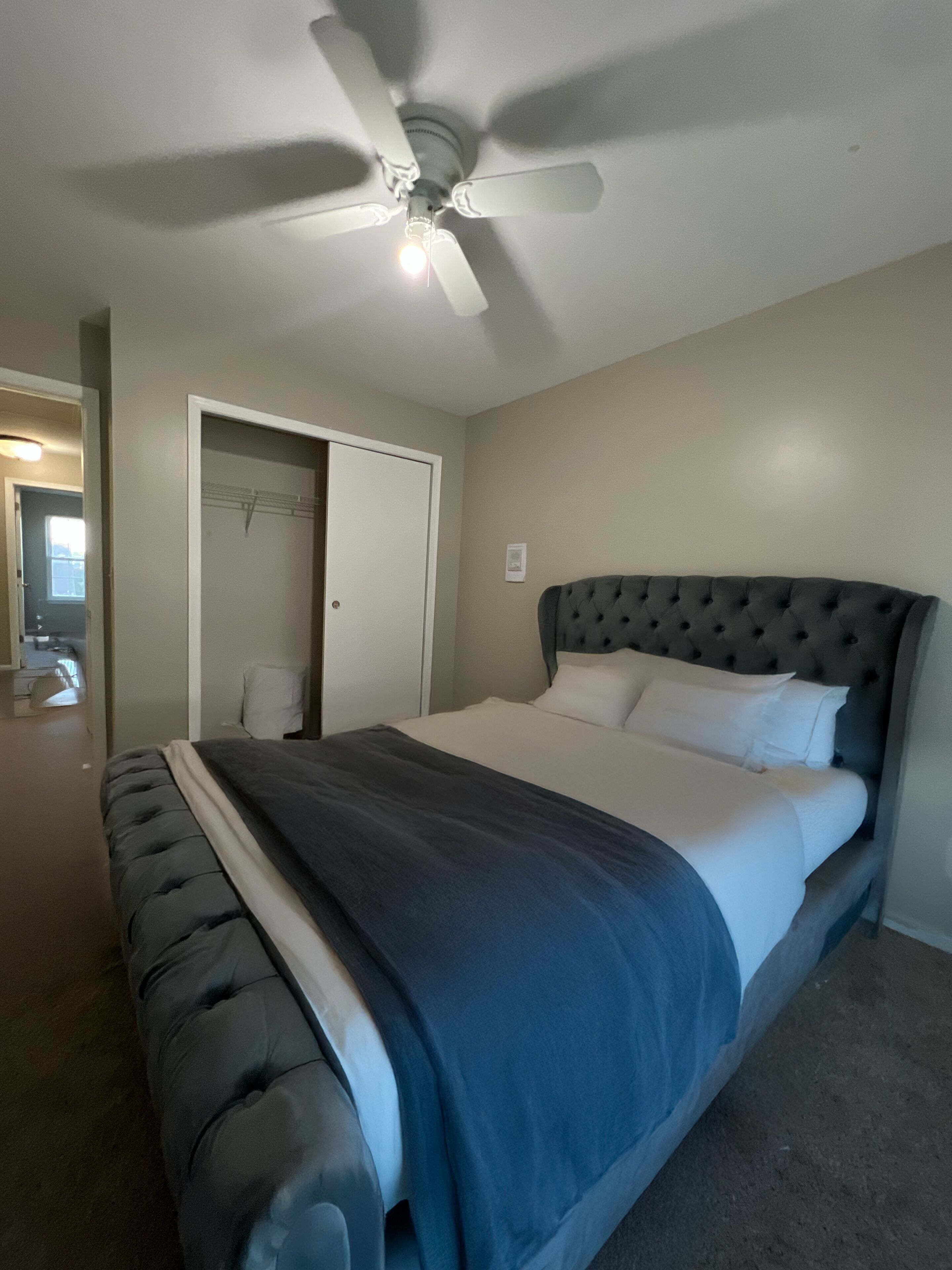 A bedroom with a bed, a ceiling fan, a door, and a light fixture.