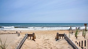 Une plage avec des passerelles en bois menant à l’eau, une plage de sable et l’océan en arrière-plan.