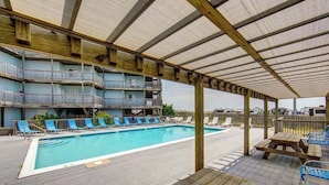 Un espace piscine avec des chaises longues bleues, une terrasse en bois et un coin salon abrité.
