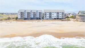Un hôtel en bord de mer, doté de plusieurs étages et de balcons, situé près du rivage, là où les vagues viennent s’écraser sur la plage.
