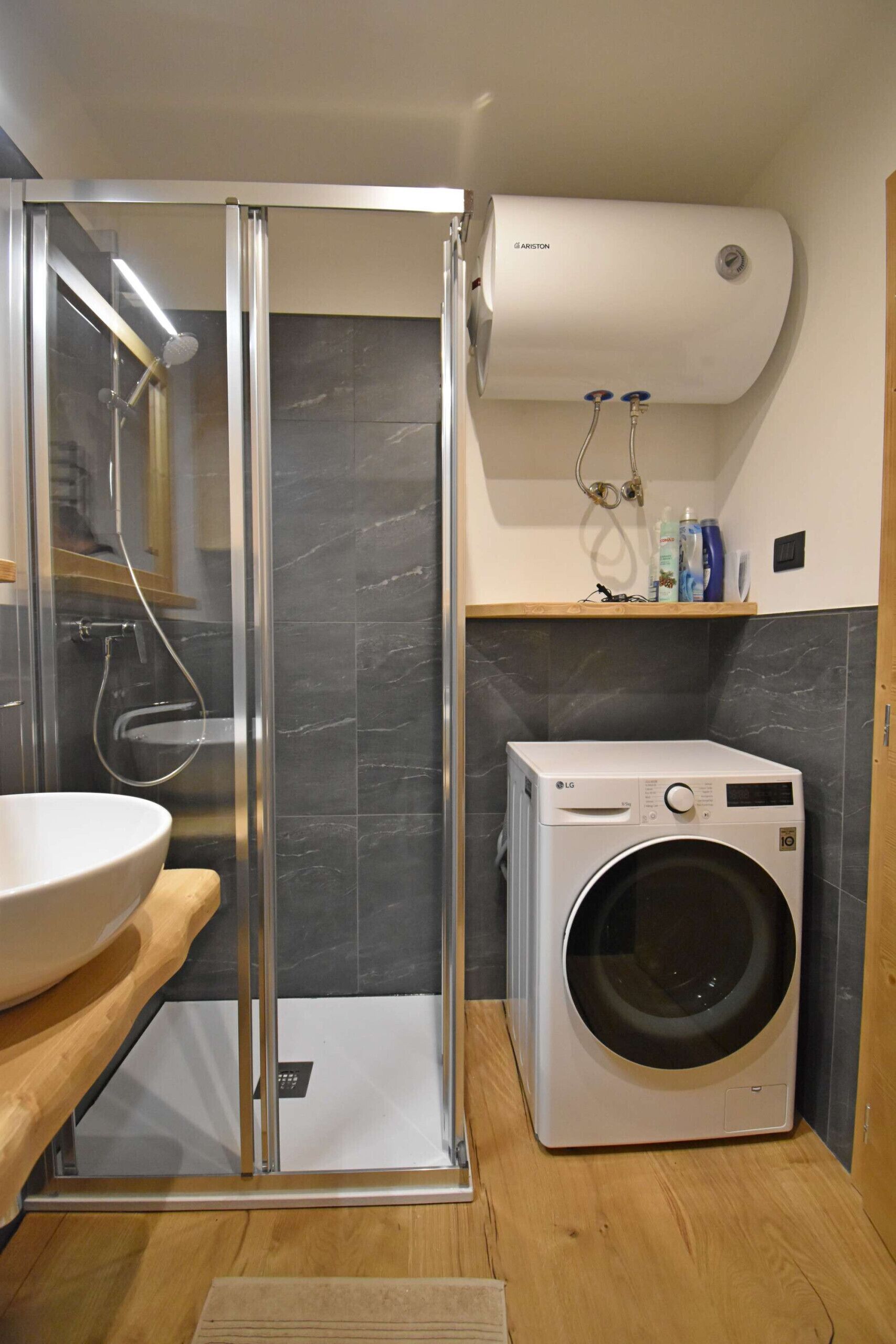 A modern bathroom with a glass-enclosed shower, a built-in sink, a wall-mounted air conditioner, and a front-loading washing machine.