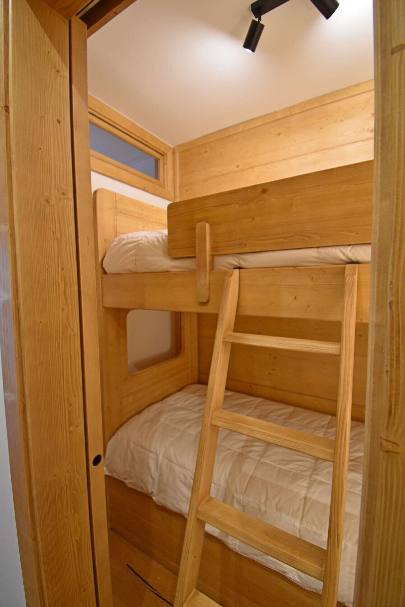 Un lit superposé avec une échelle, des murs en bois et une fenêtre.