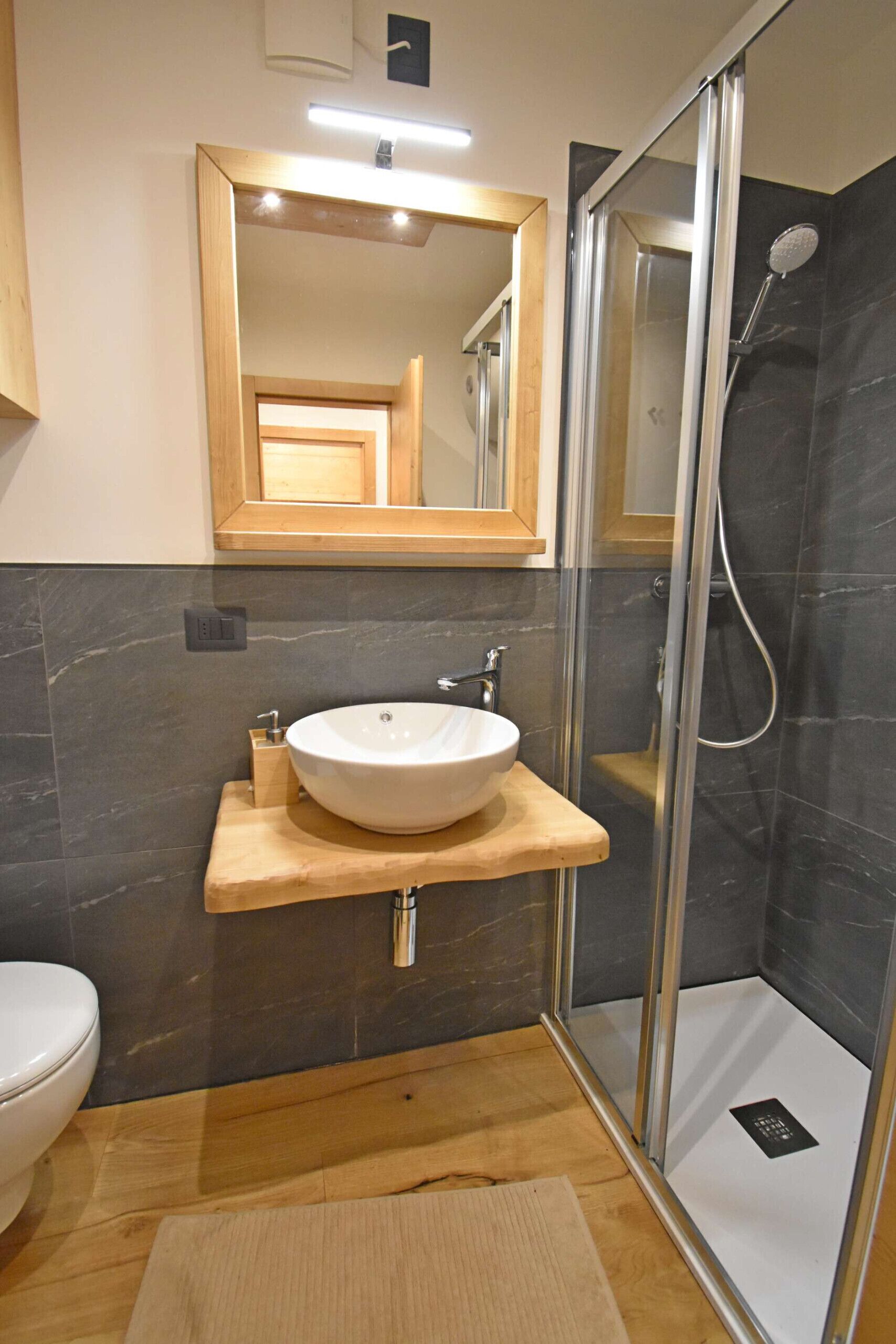 A modern bathroom with a wooden vanity, a white sink, and a glass-enclosed shower.