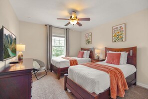 A hotel room with two beds, a desk, a chair, a ceiling fan, and artwork on the walls.