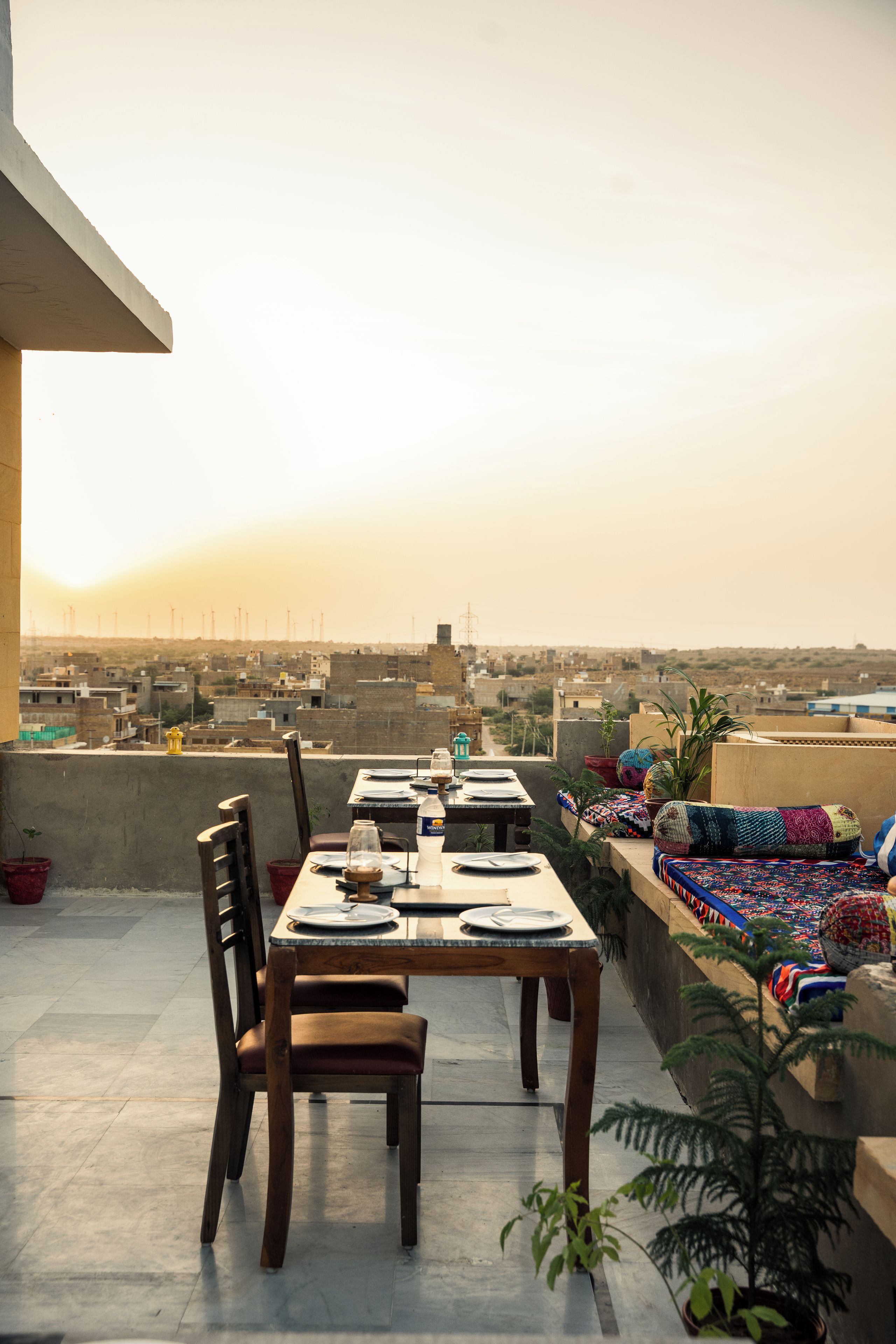 Una terraza en la azotea con una mesa para dos, sillas y vistas a un paisaje urbano con aerogeneradores a lo lejos.