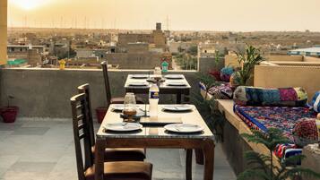 Una terraza en la azotea con una mesa para dos, sillas y vistas a un paisaje urbano con aerogeneradores a lo lejos.