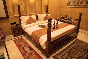 Una cama con dosel de madera, ropa de cama blanca y almohadas decorativas. Se ve una mesita de noche con un teléfono y una bandeja con botellas.