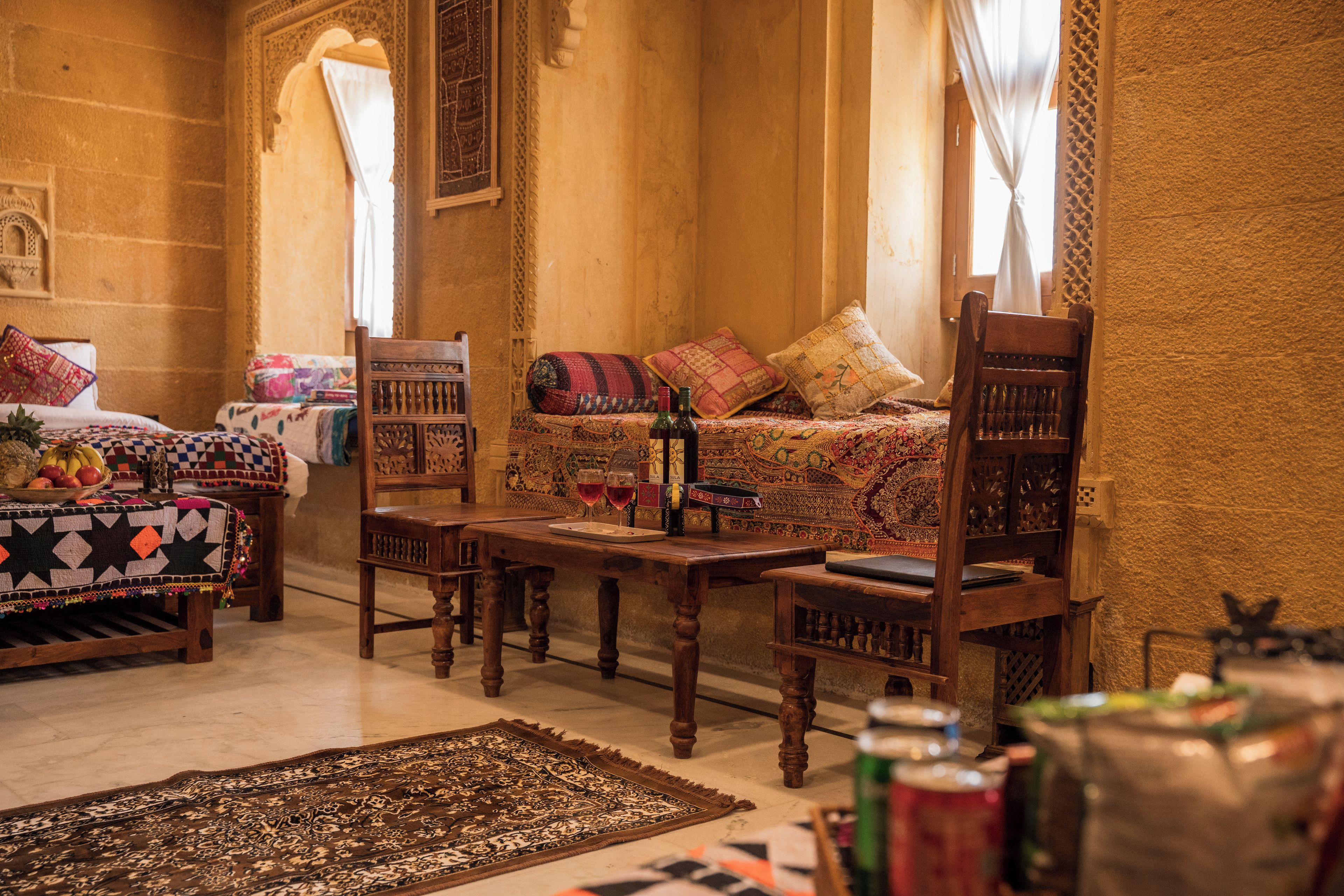 Una habitación tradicional con una cama, dos sillas de madera, una mesa y un tapete estampado.