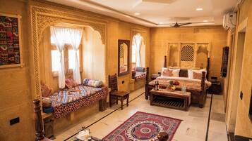Una habitación tradicional con cama, sofá, una mesa con frutera y una alfombra decorativa.
