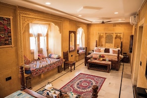 A traditional room with a bed, a sofa, a table with a fruit basket, and a decorative rug. - Hotel Desert Castle Jaisalmer (Jaisalmer)