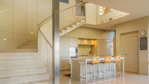 A modern kitchen with a central island, stainless steel appliances, and a staircase leading to an upper level. - Bay View Escape - Whitianga Holiday Home (Whitianga)