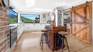 A modern kitchen with a large window, white cabinets, a brick wall, and a wooden wine rack. - Kakepuku View and Spa Retreat - Te Awamutu (Te Awamutu)