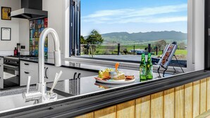 A modern kitchen with a large window overlooking a scenic landscape. - Kakepuku View and Spa Retreat - Te Awamutu (Te Awamutu)