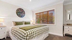Een slaapkamer met een groot bed, een ronde wanddecoratie, een raam met zonwering, een nachtkastje en een dressoir.