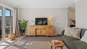 Een woonkamer met een houten kast, een televisie, een bank, een lamp en een plant.