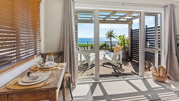 Een balkon met uitzicht op de zee, een houten tafel gedekt met borden en glazen, en een rieten mand met brood.