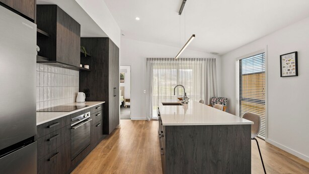 Een moderne keuken met donker houten kastjes, een centraal kookeiland en uitzicht op de eethoek.