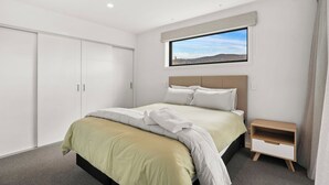 Een slaapkamer met een bed, nachtkastje, kledingkast en een raam met uitzicht op het landschap.