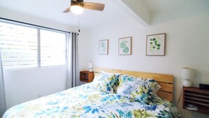 A bedroom with a bed, a ceiling fan, a window with blinds, and three framed pictures on the wall.