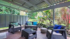 An outdoor patio area with wicker furniture, a small table with a plant, and a covered ceiling with string lights.
