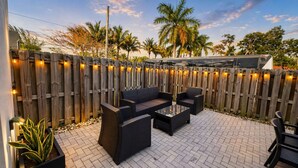 An outdoor patio with a wooden fence, black wicker furniture, and a potted plant. - Stylish Stay Near Hard Rock Stadium (North Miami Beach)