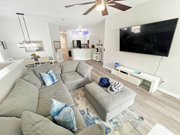 A modern living room with a sectional sofa, a flat-screen TV, and a ceiling fan. - Bright and contemporary resort property - Recently updated/themed - within 10 mins of Disney (Kissimmee)