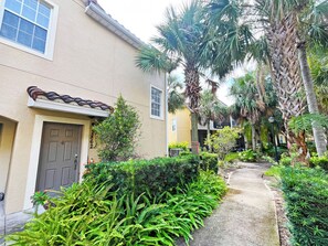 A residential building with a beige exterior, a dark brown door, and a small garden with ferns and palm trees. - Bright and contemporary resort property - Recently updated/themed - within 10 mins of Disney (Kissimmee)