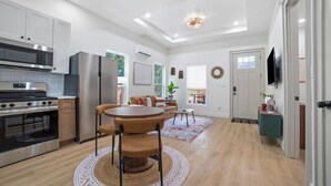 Una cocina moderna con electrodomésticos de acero inoxidable, una zona de comedor con una mesa redonda y sillas, y una sala de estar con sofá y televisor.