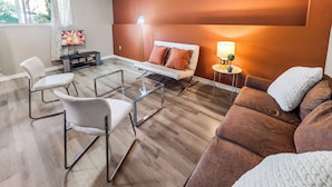 Un salon moderne avec un canapé, des fauteuils, une table basse en verre, une lampe et un téléviseur.